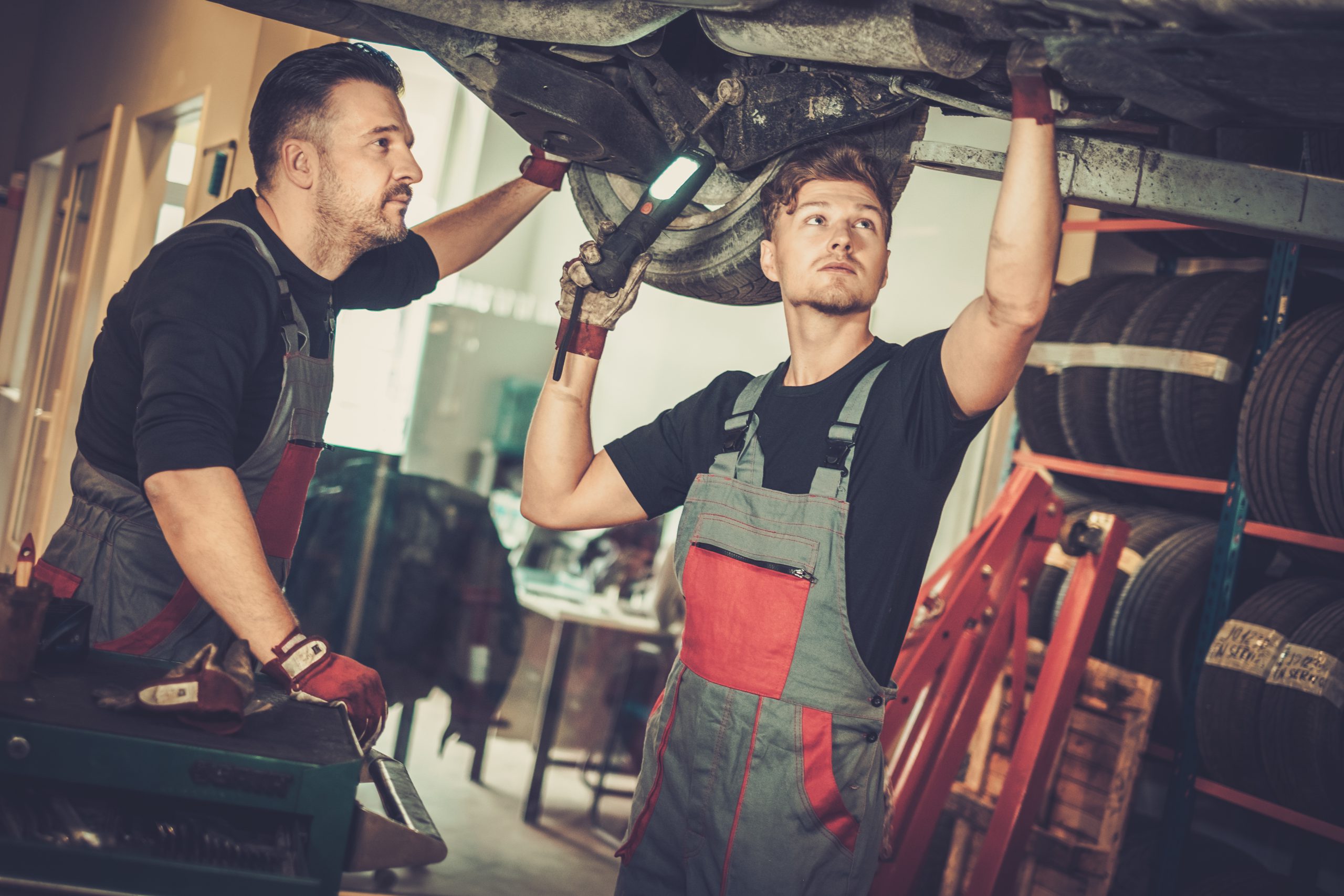 Professional car mechanics working under lifted car in auto re
